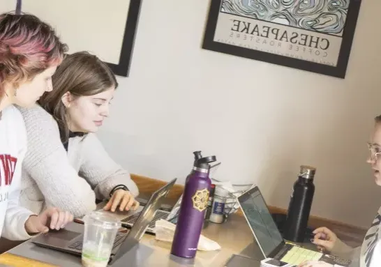 Three students with laptops at a table